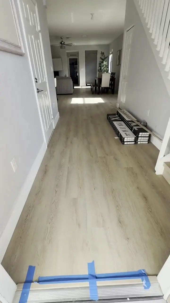 Plank flooring going down a hallway, remaining boxes stacked along the wall and painter&rsquo;s tape across the threshold