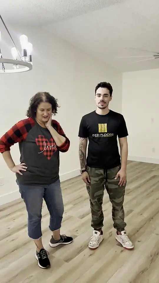 A homeowner standing with someone from Ozzifloors on her finished grey-brown plank floor, under the chandelier