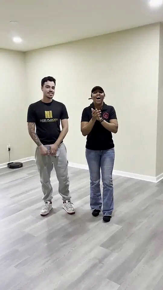 A homeowner applauding beside someone from Ozzifloors in her empty room, on the new grey plank floor