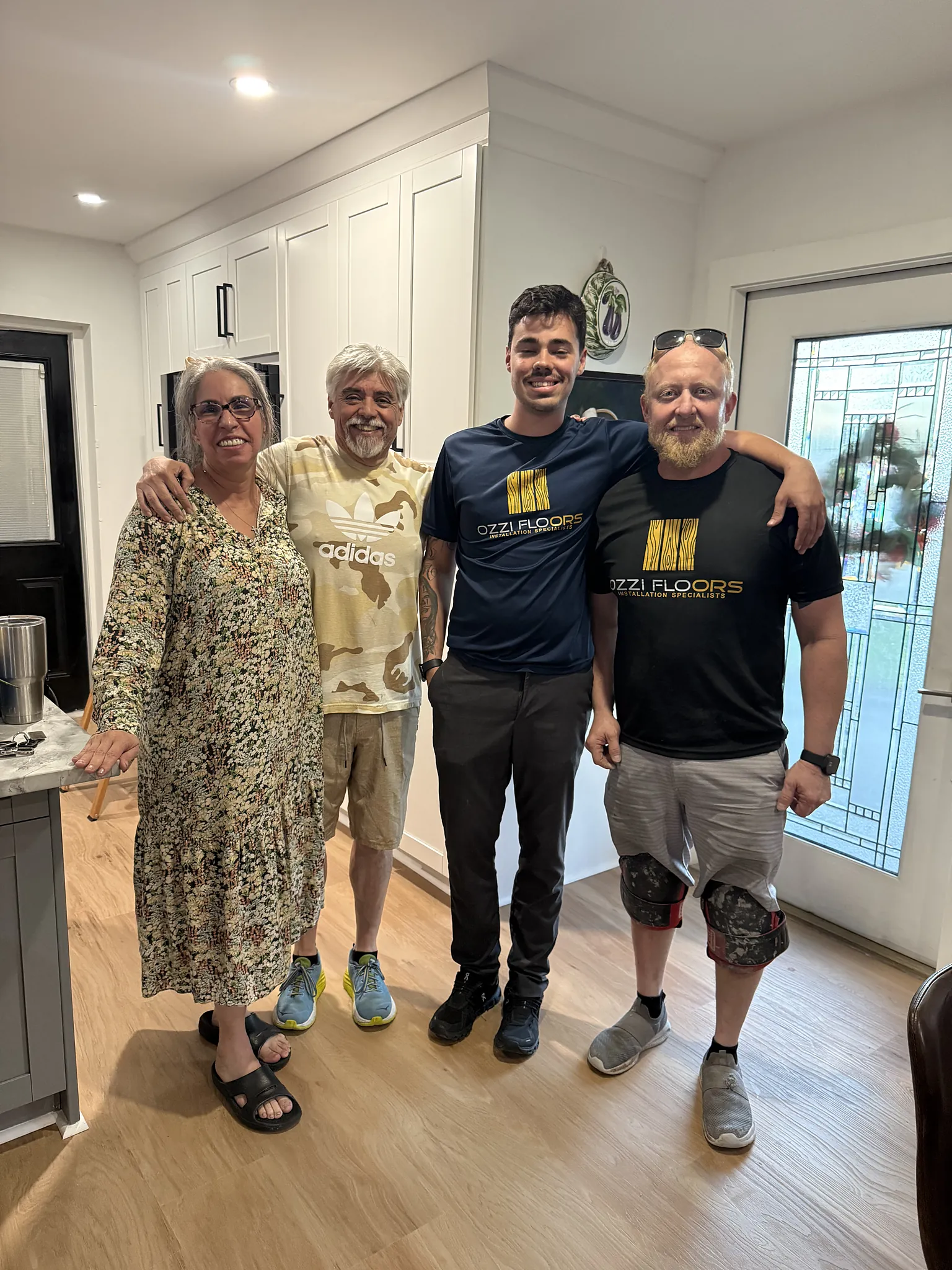 Two homeowners standing with the Ozzifloors crew on their finished floor by the front door
