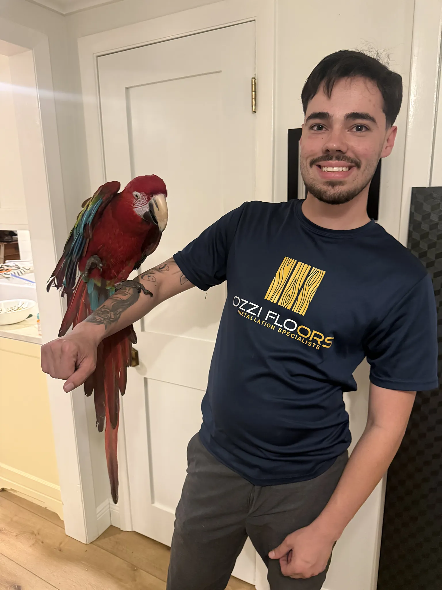 Walter of Ozzifloors, in the company shirt, smiling with a parrot perched on his arm
