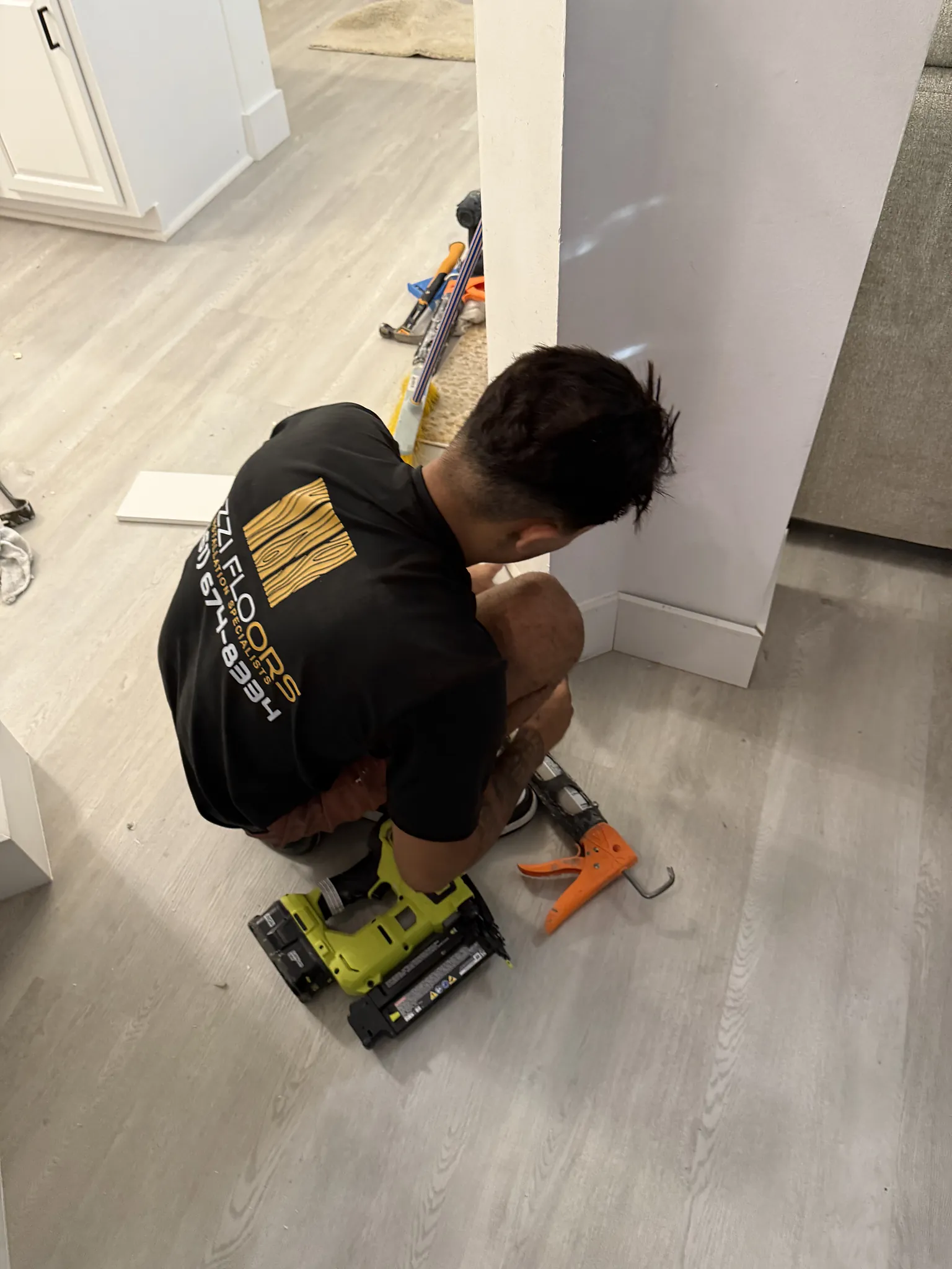 Ozzifloors installer cutting trim on the floor of a room finished in pale plank