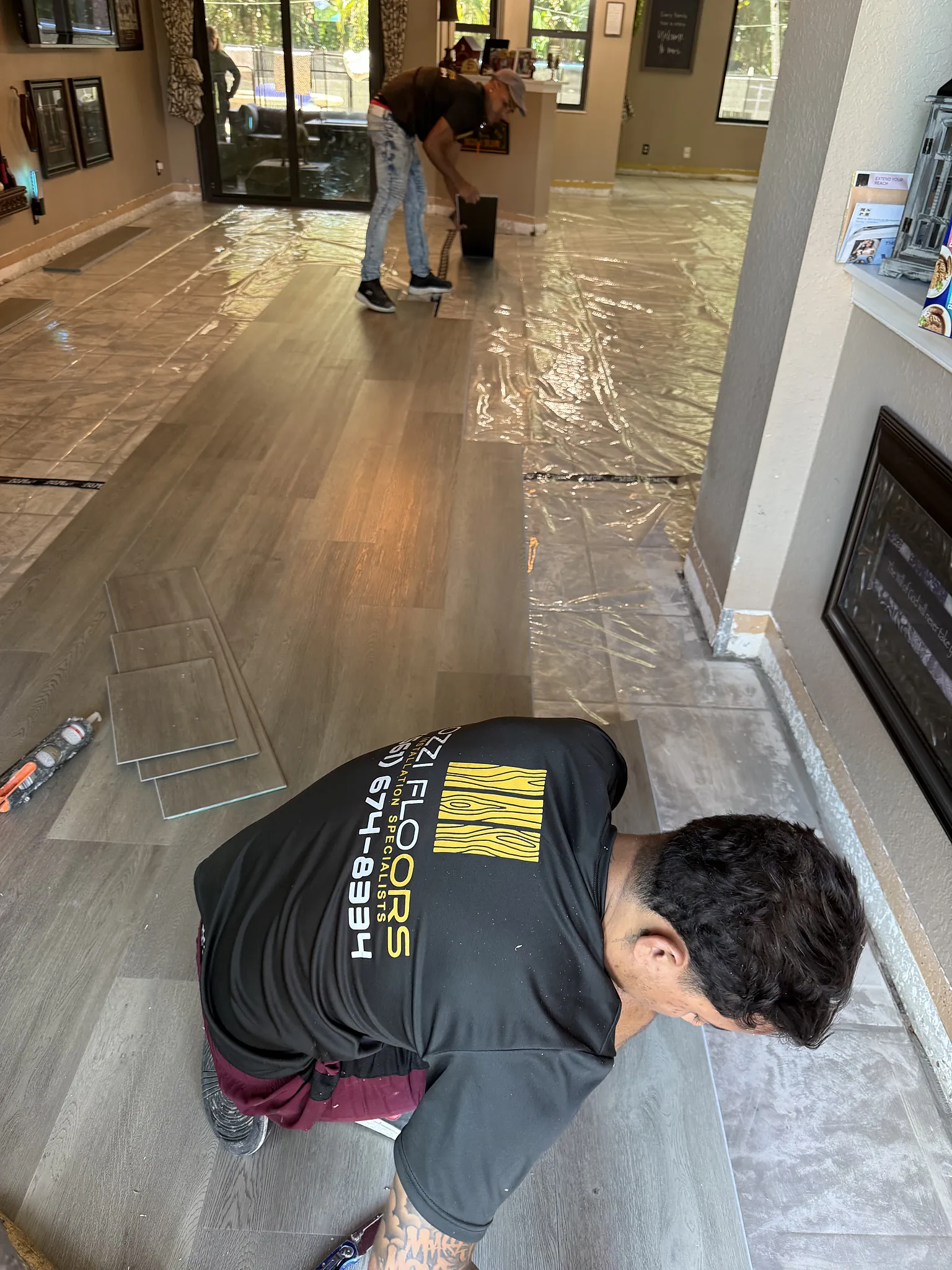 Ozzifloors installer laying plank flooring in a living room, the new floor protected as it goes down