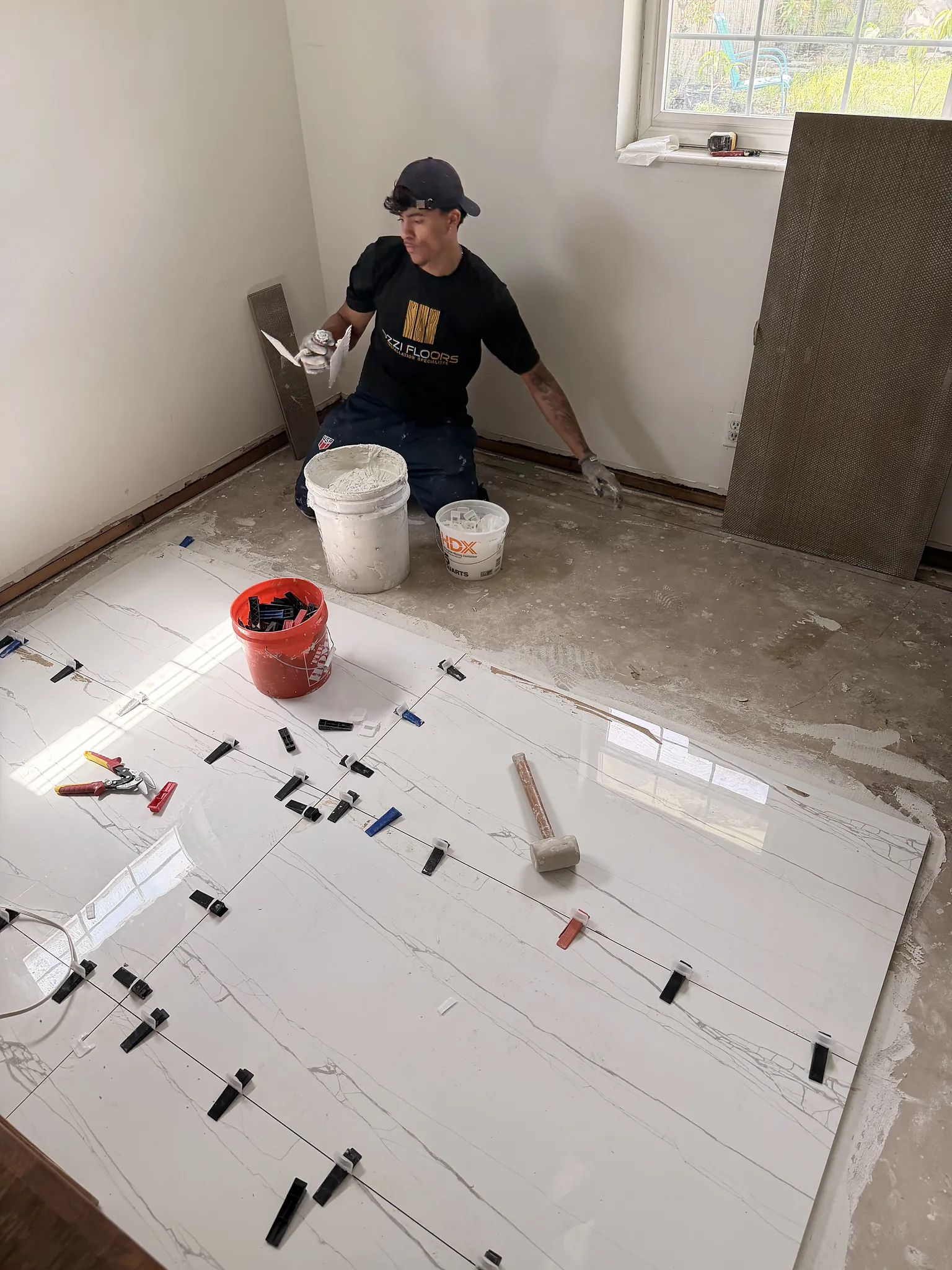 An Ozzifloors setter laying large white marble-look tiles with leveling clips