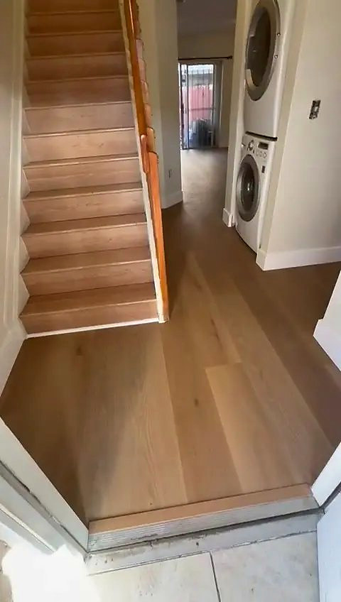 A finished stair run meeting the plank floor at a laundry doorway, installed by Ozzifloors